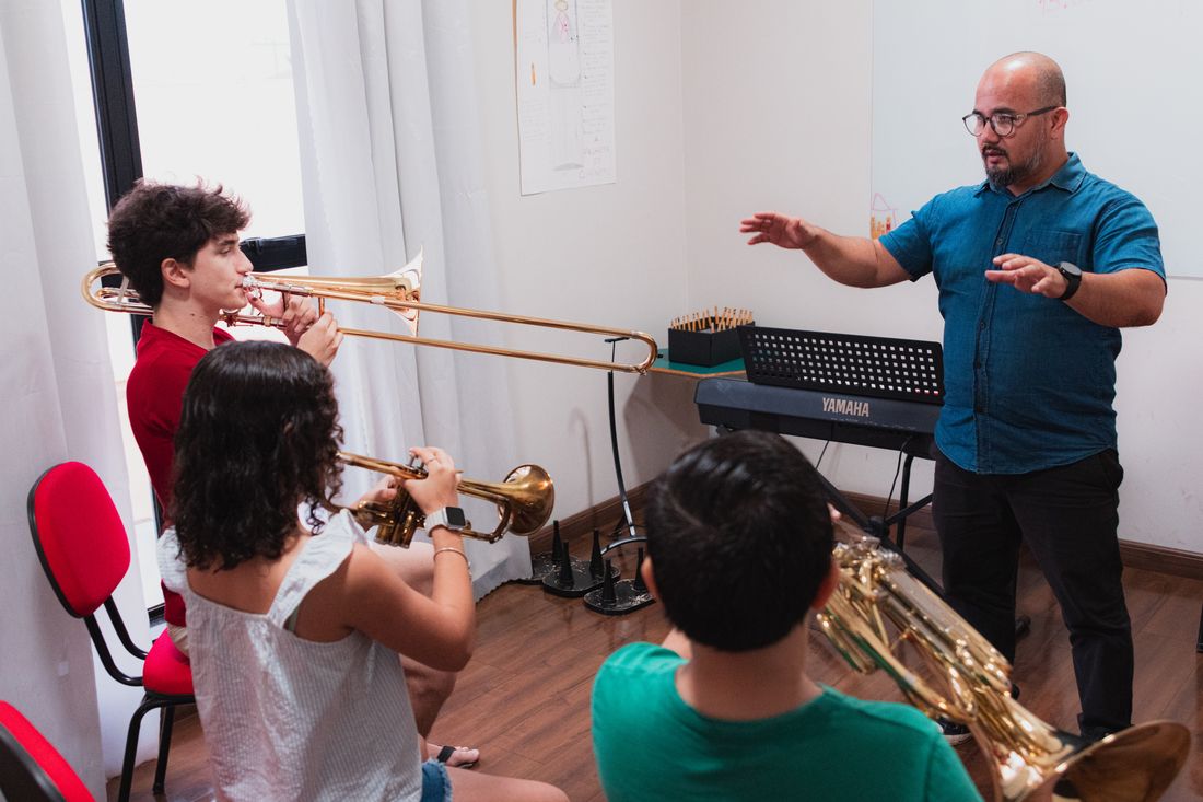 Aula de trombone e trompete com professor regendo jovens músicos