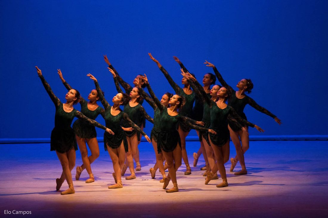 Bailarinas do Filadelfia Dance em coreografia de braços erguidos, fundo azul